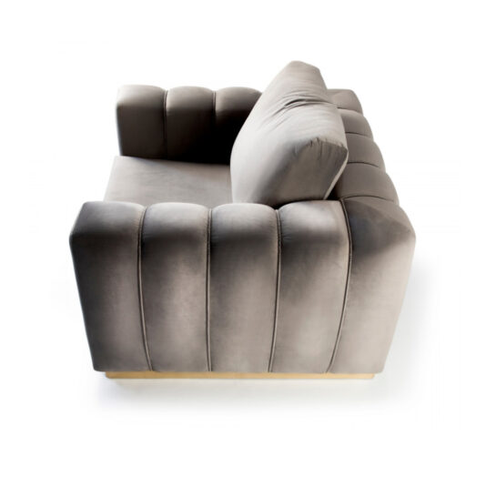 The Exclusive Modern Armchair is showcased with its plush, grey velvet upholstery and wide, cushioned armrests and backrest. The vertical quilting and low wooden base lend it a sophisticated look, while the angled side perspective highlights its luxurious design against a white background.