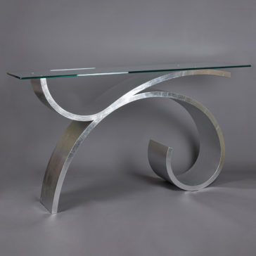 Exclusive Silver Leaf Console Table A modern console table featuring a sleek, curved metallic base and a glass top. The base consists of a large, artistic swirl design, giving the table a contemporary and artistic appearance against a plain gray background—an ideal choice in how to choose the perfect console table.
