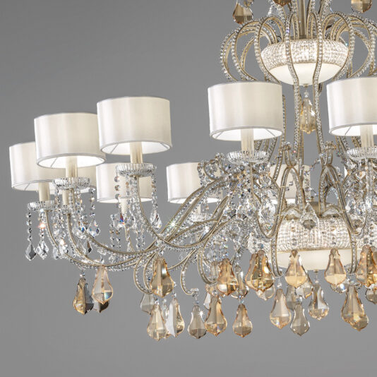 Large Crystal Chandelier With Shades The Large Crystal Chandelier With Shades boasts intricate metalwork, crystal accents, and cascading teardrop-shaped crystals, each adorned with a white lampshade encircling an individual light bulb. This opulent piece enhances elegance against a neutral gray backdrop.