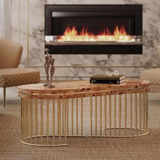 A modern living room featuring the Modern Burl Veneer Coffee Table with a golden metal base, adorned with a small sculpture and stacked books. Two beige armchairs sit on either side, and a sleek electric fireplace with a white marble surround is mounted on the wall.