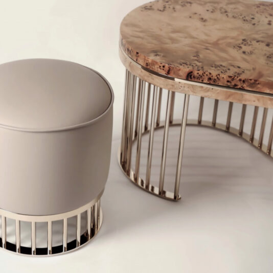 Modern Burl Veneer Coffee Table Introducing the Modern Burl Veneer Coffee Table—a sophisticated wooden circular table showcasing an exquisite burl veneer surface. Accompanied by a matching cylindrical cushioned stool, both pieces feature sleek, vertical metal bar bases that contribute to a minimalistic aesthetic in a neutral color palette.