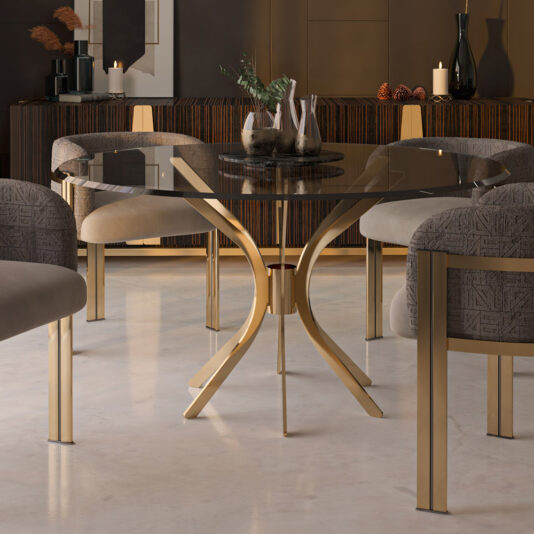A contemporary dining room highlights the Modern Round Glass Dining Set with a gold metal base, encircled by grey cushioned chairs. At its heart, vases brimming with greenery introduce a hint of nature. The room's chic decor is enhanced by gently glowing candles and dark wooden accents in the backdrop.