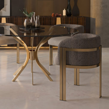 Modern Round Glass Dining Set A contemporary dining room showcasing the Modern Round Glass Dining Set, which includes a sleek round glass table with gold legs and four upholstered chairs featuring gold frames. The room is adorned in a neutral beige and brown color scheme, while decorative items like plants, a candle, and pinecones adorn a buffet in the background.