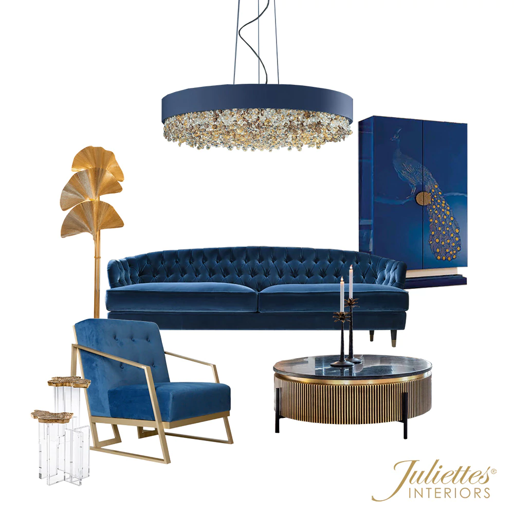 A luxurious living room setup reminiscent of the grandest rooms of Queen Elizabeth, featuring a blue velvet tufted sofa, matching blue velvet armchair with gold accents, round coffee table with fluted base, gold leaf floor lamp, blue peacock artwork, and a crystal-detailed chandelier. Branding: Juliette’s Interiors.