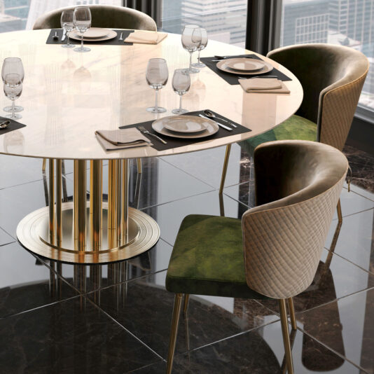A modern dining table surrounded by four stylish Quilted Dining Chairs. The table features a glossy, cream-colored round top and a gold pedestal base. Place settings with plates, cutlery, napkins, and empty wine glasses are arranged on black placemats.
