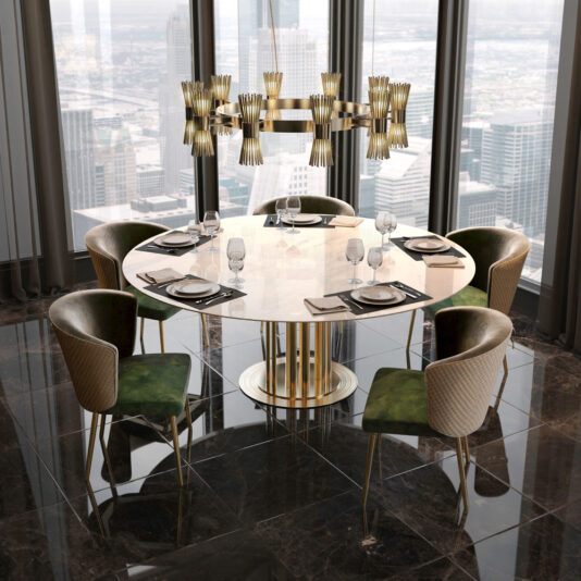 A modern dining room highlights a round table adorned with a marble top and golden accents, complemented by six Quilted Dining Chairs in an elegant green and gold. The table is beautifully set with plates, glasses, napkins, and cutlery. Above, a large and elaborate chandelier illuminates the space. Tall windows provide an impressive view of the cityscape.