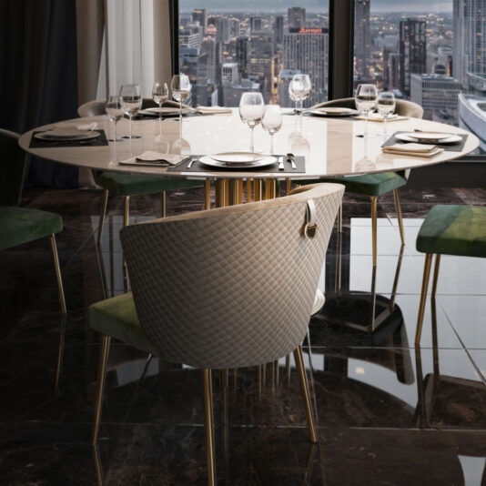 A modern dining room showcases the Round Marble Dining Table and Chairs Set, perfectly arranged for a meal with white plates, wine glasses, and black napkins placed on its glossy marble surface. The table is elegantly surrounded by six chairs featuring green upholstery and gold-colored legs. Large windows provide a stunning view of the cityscape outside.