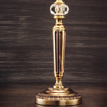 Traditional Gold Plated Table Lamp A close-up view of a vintage brass candlestick holder with an ornate design and a crystal accent near the top, standing on a dark wooden surface and set against the Traditional Gold Plated Table Lamp background.