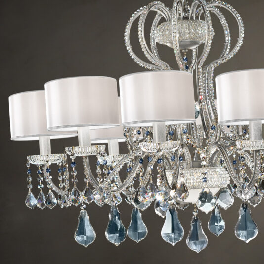 A close-up view of the Traditional Italian Crystal Chandelier reveals intricately designed crystal-adorned arms and large teardrop-shaped prisms. It features multiple white fabric lampshades and exquisite detailing, with the crystals reflecting light to create a mesmerizing sparkling effect.