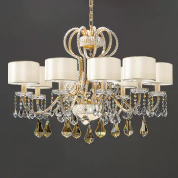 A Classic Crystal Chandelier With Shades and a gold frame, adorned with numerous crystal droplets, hangs elegantly from the ceiling. It features six white lampshades evenly spaced in a circular arrangement, each supported by an ornate, curving arm. The background is a solid dark gray.