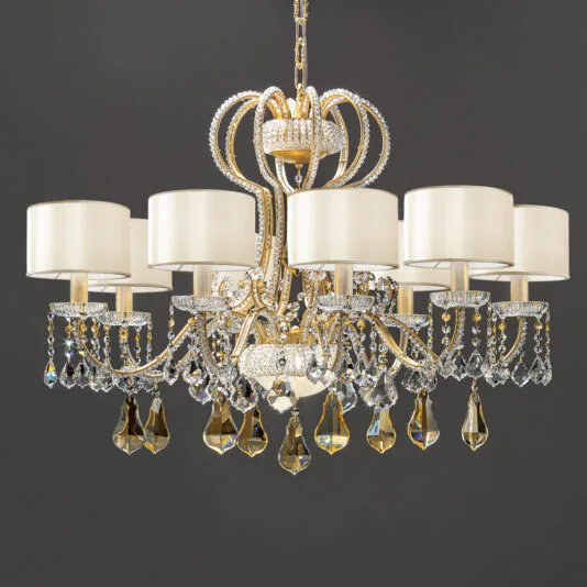 A Classic Crystal Chandelier With Shades and a gold frame, adorned with numerous crystal droplets, hangs elegantly from the ceiling. It features six white lampshades evenly spaced in a circular arrangement, each supported by an ornate, curving arm. The background is a solid dark gray.