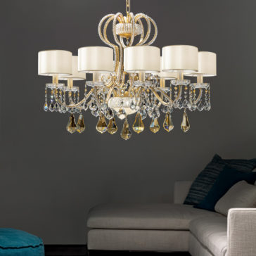 The Classic Crystal Chandelier With Shades, featuring multiple candle-shaped lights adorned with crystals, hangs from the ceiling in a modern living room with a grey sofa and teal cushions. The dark background wall enhances the elegant lighting fixture's glow.