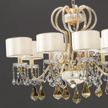 The Classic Crystal Chandelier With Shades is an ornate, gold fixture adorned with hanging crystal droplets and fabric lampshades. Featuring multiple arms, each holding a light, this chandelier adds an elegant and luxurious touch to any space.
