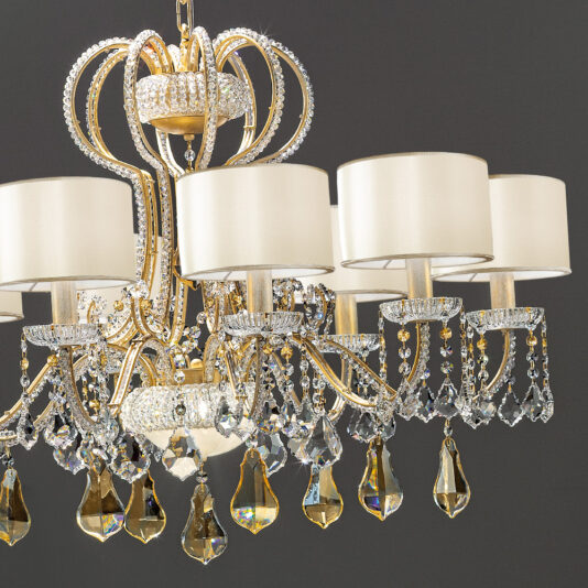 Classic Crystal Chandelier With Shades The Classic Crystal Chandelier With Shades is a luxurious piece featuring an elegant gold and crystal design with eight arms adorned with cream-colored lampshades. The chandelier is decorated with sparkling crystal beads and large teardrop-shaped pendants, creating a sophisticated ambiance against a dark gray background.