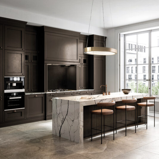 The modern kitchen features dark cabinetry, a marble island with bar stools, and a Contemporary Oval Chandelier. Sunlight streams through large windows, illuminating the spacious area with an outdoor view.