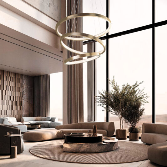 Tall windows and soft lighting highlight circular sofas encircling a central coffee table on a round rug in the modern living room. A large plant is near the window, while a Contemporary Round Tiered Chandelier enhances the minimalist and elegant decor from the ceiling.