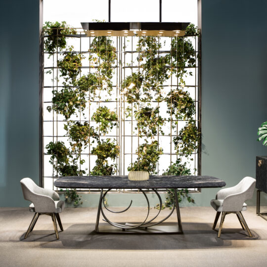 A modern dining area features the Large Modern Bronze Dining Table with a sleek, curved metal base and two upholstered chairs. A vertical garden grid on the wall introduces vibrant greenery to the contemporary space.