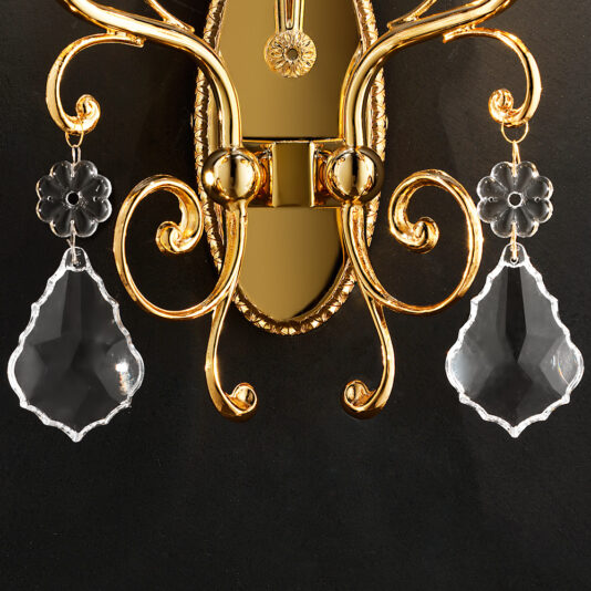 A detailed view of the Classic Crystal Pendant Wall Light showcases its intricate curved designs. The elegant gold sconce boasts two clear, teardrop-shaped crystal pendants on each side. Set against a black background, the gold and crystal elements are accentuated beautifully.