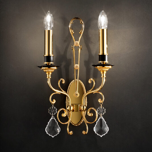 The Classic Crystal Pendant Wall Light is designed with a gold wall sconce that supports two candle-style light fixtures. Each fixture is topped with a clear bulb and adorned with intricate decorations and crystal pendants, all set against a dark backdrop to add an elegant and sophisticated touch.
