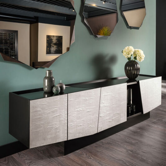 A Contemporary 4 Door Sideboard with textured, metallic finish doors is set against a teal wall. Above it, three geometric mirrors are mounted. Decorative vases and a dark vase filled with white flowers adorn the top of the sideboard, which rests on modern wood flooring.