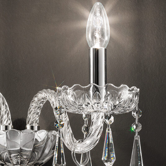Contemporary Crystal Pendant Wall Light A close-up of an elegant Contemporary Crystal Pendant Wall Light illuminated by a single bulb. The fixture showcases intricate glass detailing and hanging contemporary crystal pendants, set against a dark background. The light beautifully catches the crystals, creating a sparkling effect.