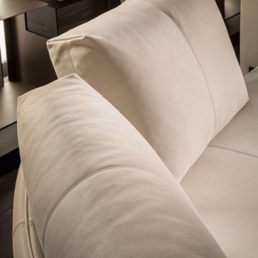 Close-up of the Contemporary Leather Modular Corner Sofa in beige leather, featuring a plush cushion and headrest. The smooth and comfortable upholstery showcases subtle stitching details. The background reveals parts of wooden furniture and ambient indoor lighting.