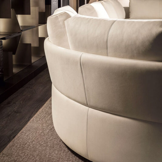 A close-up of the Contemporary Leather Modular Corner Sofa in a modern cream color, featuring oversized cushions. The sofa boasts a smooth texture and is placed next to a dark, patterned wall and wooden floor, creating a stylish, contemporary living space.
