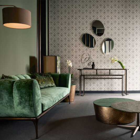 Contemporary Luxury Sofa A stylish living room showcasing the Contemporary Luxury Sofa in green velvet, a round metallic coffee table with a hammered texture, and a console table placed against a geometric patterned wall. Three circular mirrors are artfully hung on the wall, and the room is illuminated by a modern pendant lamp.