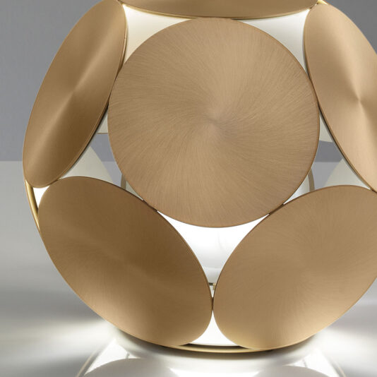 The Contemporary Metal Disc LED Table Lamp showcases a unique design with overlapping metallic circular discs in a brushed gold finish, allowing light to emanate from the gaps. The lamp sits on a reflective white surface against a light grey background.