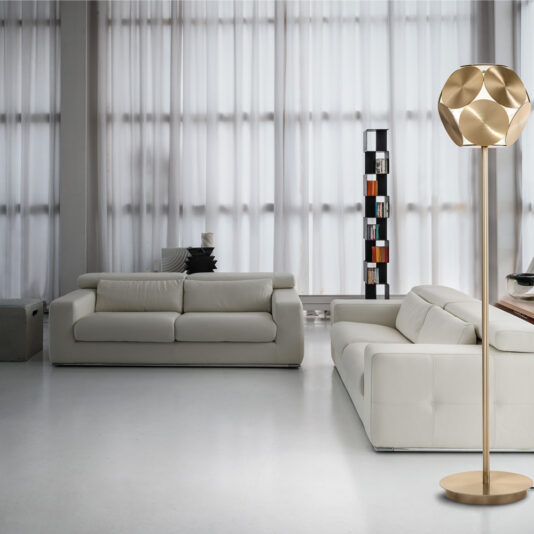 A modern living room featuring two white leather sofas, a Contemporary Metal Disc LED Floor Lamp adorned with a geometric shade, and a tall narrow bookshelf positioned against large windows draped with sheer white curtains. The room exudes a minimalist design characterized by its clean and bright appearance.