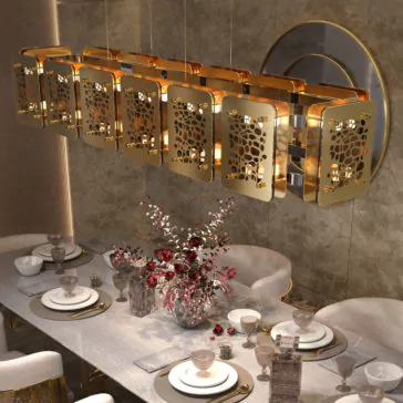 A modern dining room is illuminated by the Contemporary Rectangular Chandelier, which features intricately designed gold panels. The table, set for six, showcases elegant white and gold dinnerware, sparkling crystal glasses, and a floral centerpiece with vibrant red flowers. The backdrop includes a large round mirror and beautifully textured walls.