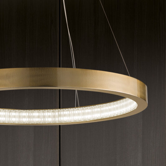 The Contemporary Round Chandelier, featuring a sleek modern design with a circular brass finish and built-in LED lights, is suspended by thin wires against a dark wood-paneled background. Its minimalist aesthetic beautifully highlights the fixture's contemporary elegance.