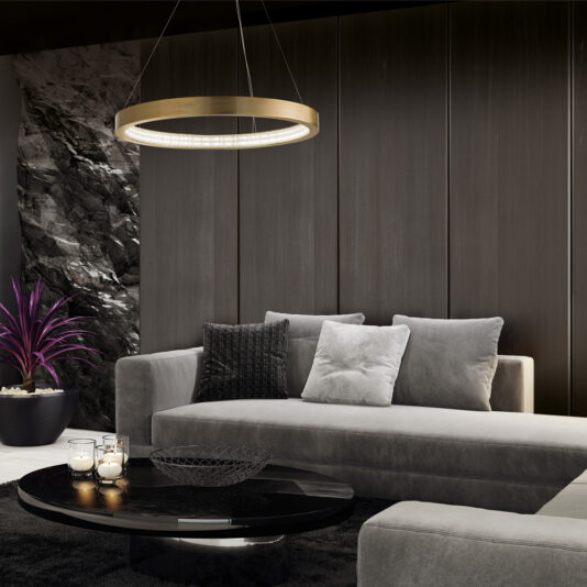 A modern living room features a gray velvet sectional sofa adorned with decorative pillows, a black circular coffee table, and a Contemporary Round Chandelier with a golden finish. A potted plant with purple leaves sits in the corner, while large dark panels cover the wall.