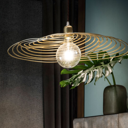 The Contemporary Spiral Chandelier showcases a large, exposed bulb enveloped in a distinct golden wire design. It is suspended in front of a dark-colored wall with a green plant placed in a ceramic vase in the background, infusing the setting with a touch of nature.