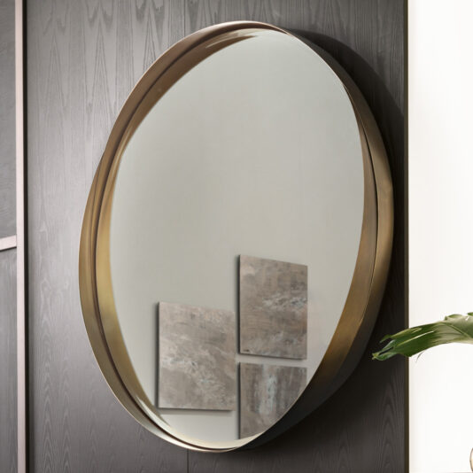 An elegant oval mirror with a thin, gold-colored frame is mounted on a dark wood-paneled wall. The reflection reveals two abstract paintings and a portion of a green leafy plant, exuding a modern and sophisticated aesthetic similar to that of the Contemporary Twisted Bronze Round Mirror.