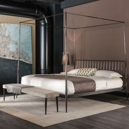 Contemporary Upholstered Bench A modern bedroom features a sleek metal four-poster bed with a white mattress, grey bedding, and decorative pillows. At the foot of the bed sits the Contemporary Upholstered Bench on a beige rug. Industrial elements, including an exposed air duct, complement the minimalist decor.