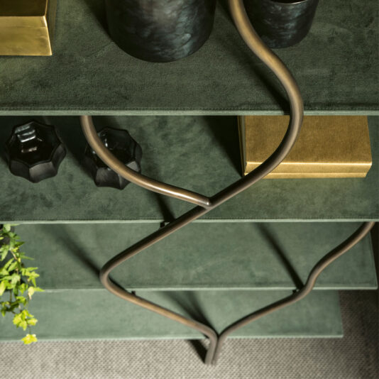 Contemporary Wrought Iron Bookcase A top-down view of the Contemporary Wrought Iron Bookcase featuring three green shelves adorned with two dark, textured vases, a gold-colored box, and two small black geometrically shaped objects. The design is enhanced by an integrated winding metal rod, and a small plant can be seen in the bottom left corner.