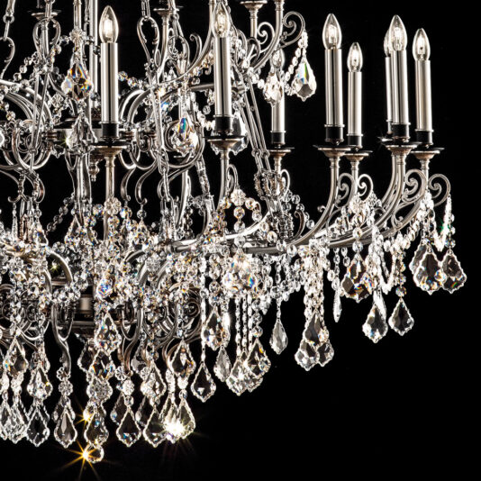 Deluxe Crystal Pendant Chandelier A close-up of the Deluxe Crystal Pendant Chandelier showcases its numerous intricately designed arms and candle-shaped light bulbs. The chandelier boasts a complex arrangement of sparkling crystals that reflect light, creating a luxurious and elegant appearance against a black background.