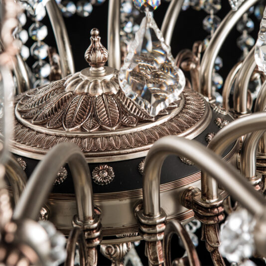 Deluxe Crystal Pendant Chandelier Close-up of the Deluxe Crystal Pendant Chandelier showcasing its intricate bronze detailing and elegant hanging crystal decorations. The image emphasizes the central metal dome adorned with etched patterns, surrounded by gracefully curved arms holding teardrop-shaped crystals.