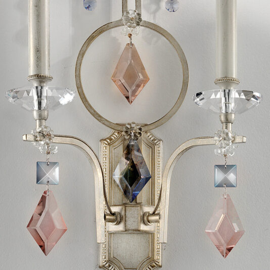 Elegant Crystal Pendant Wall Light A detailed close-up of the Elegant Crystal Pendant Wall Light showcases its vintage design. The sconce boasts two candle-like lights adorned with crystal and pink diamond-shaped pendants, adding an ornate touch. The backdrop is a simple white wall.