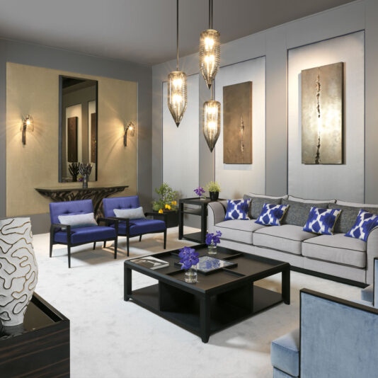 Elegant Occasional Armchair A modern living room featuring a gray couch adorned with blue and white pillows, an Elegant Occasional Armchair in deep blue, and a black coffee table. Overhead, three pendant lights hang. The room is enhanced with abstract art, a console table with a mirror, and decorative lighting sconces on the walls.
