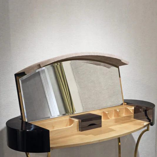 Classic Ebony Dressing Table The Classic Ebony Dressing Table is a sleek and sophisticated piece, showcasing a timeless ebony finish accented with a gold frame. It features an arched mirror that is hinged and partially open, revealing multiple storage compartments within the wooden tabletop. This elegant dressing table also includes black curved side panels and stands gracefully against a neutral wall.