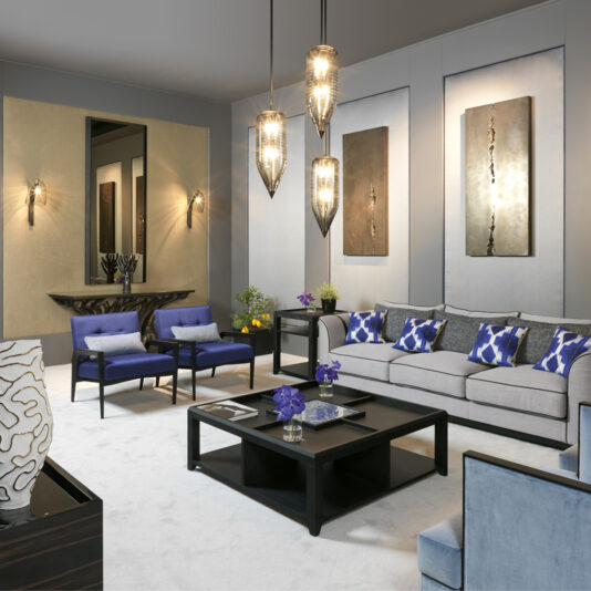 A modern living room with gray walls and carpeting features a Luxury Square Coffee Table. The space is furnished with a gray sofa adorned with blue and white pillows, two blue armchairs, and illuminated by three pendant lights hanging from the ceiling. Two abstract metal wall art pieces add a creative touch to the walls.
