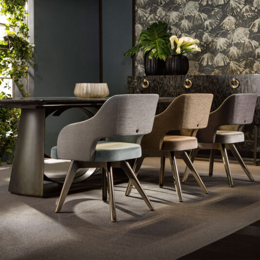 A contemporary dining space showcasing the Large Modern Bronze Dining Table Set, which includes four cushioned chairs in hues of gray and beige arranged around a sleek, expansive bronze table. A sideboard behind the chairs is adorned with potted plants and decorative items, all set against a dark, nature-inspired wallpaper backdrop.