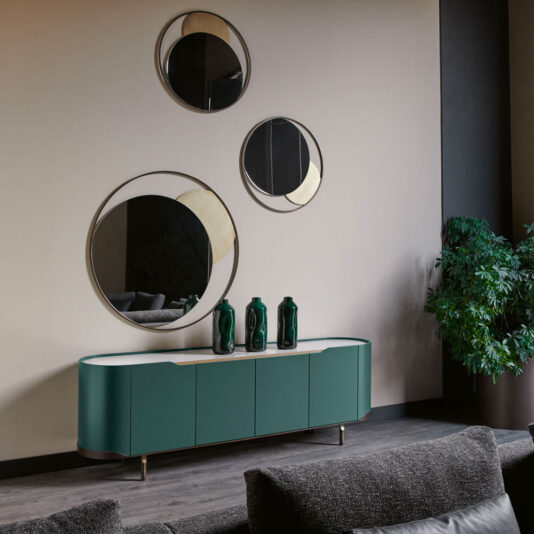 Large Modern Curved Buffet Sideboard A modern living room showcases a stylish Large Modern Curved Buffet Sideboard in chic green with white accents. Neatly placed on top are three decorative green vases. Above the sideboard, three round mirrors of varying sizes are mounted on the wall. A leafy plant occupies the corner, while sofas grace the foreground.