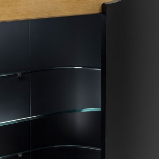 Close-up of the Large Modern Curved Cabinet, showcasing its elegant curved glass door, black side panels, and wooden top. The interior features glass shelves, enhanced by lighting that creates a reflective surface.