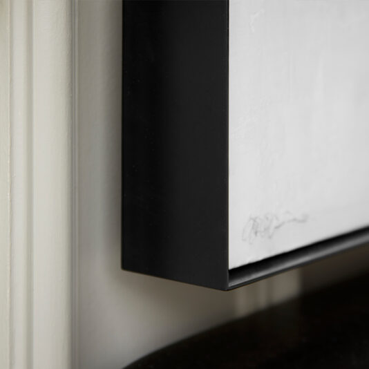 Close-up of the corner of a Luxury Abstract Artwork framed picture hanging on a light-colored wall. The frame is black with a smooth finish, enhancing the luxury feel of the artwork within. The edge of the piece shows the artist's signature, while the frame casts a slight shadow on the wall.