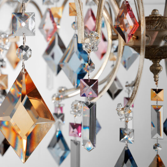 Luxury Crystal Pendant Chandelier Close-up of the Luxury Crystal Pendant Chandelier featuring an array of faceted, colorful, and translucent gem-like crystals. The crystals come in various shapes like diamonds and rectangles, hanging gracefully from metallic fixtures and reflecting light across a spectrum of colors.