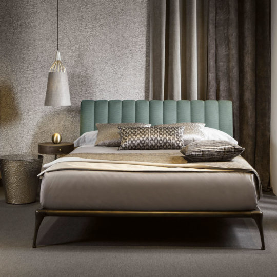 A contemporary bedroom showcases a Modern Bed With Upholstered Headboard, highlighted by its stylish light blue tufted design. The neatly made bed is adorned with decorative pillows and a neutral textured comforter. Two nightstands, including one with a unique metallic texture, flank the bed for added sophistication. A hanging pendant light injects a chic flair into the space.