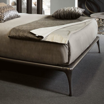 The Modern Bed With Upholstered Headboard boasts a sleek, minimalist design with an upholstered headboard. It comes complete with a gray mattress, a dark gray textured throw blanket partially folded back, and two decorative pillows—one in gray and the other in a patterned design. The bed frame is made of black metal with slender legs.